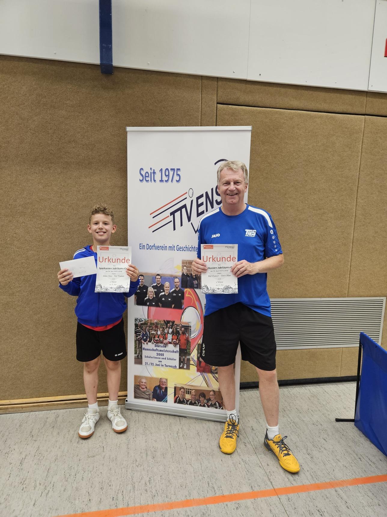 Zwei Personen mit Urkunden stehen neben einem Banner des Tischtennisvereins in einer Sporthalle.