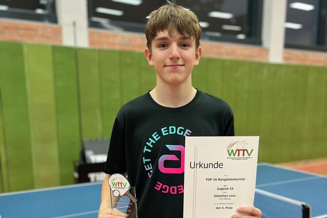 Junge mit Pokal und Urkunde am Tischtennistisch in einer Halle, im Hintergrund gr&uuml;ne W&auml;nde und Tischtennisplatte.