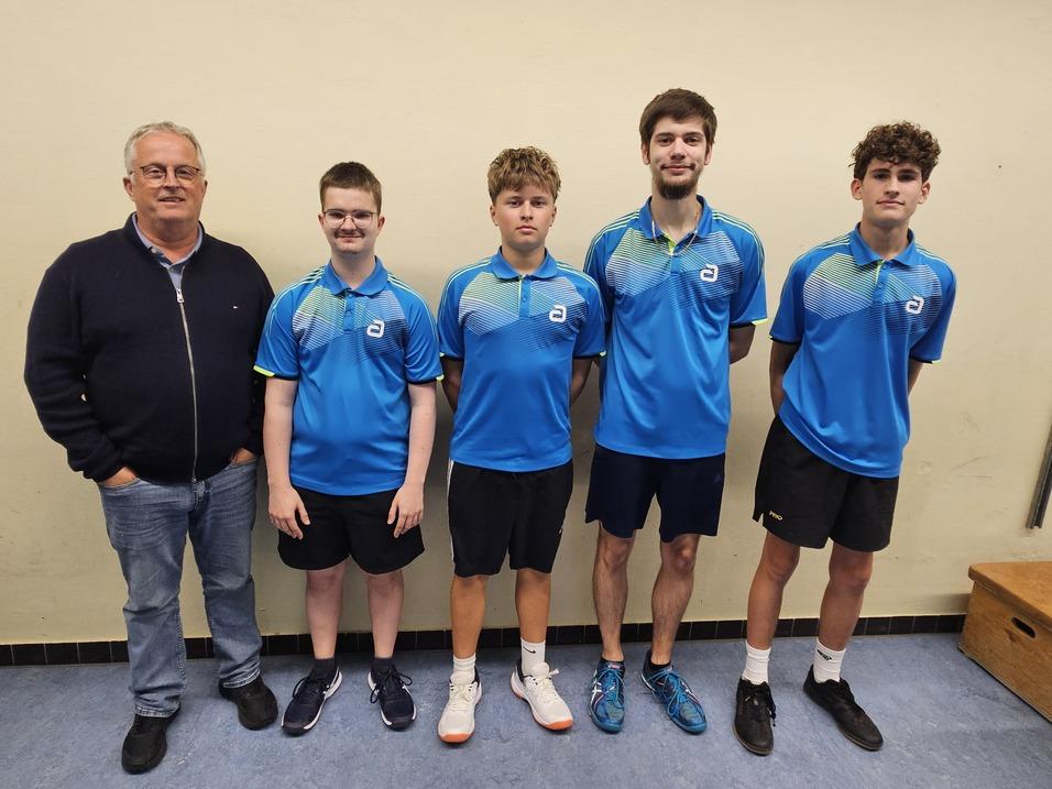 Gruppe von vier Personen in blauen Sportshirts, stehend vor einer Wand in einem Sportraum.
