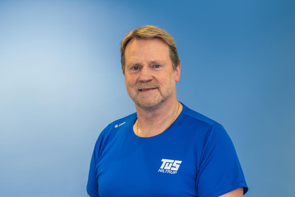Portr&auml;t eines Mannes mit kurzen, hellen Haaren in einem blauen Sportshirt vor einem einfarbigen blauen Hintergrund.
