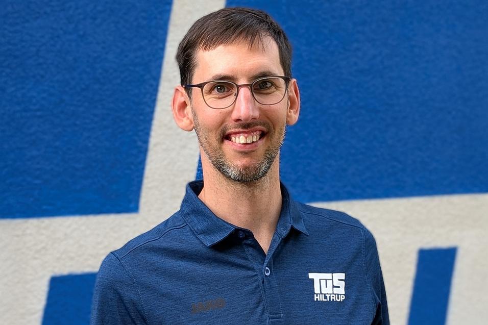 Simon Chrobak Porträt eines Mannes mit Brille in einem blauen Polohemd vor einer blauen Wand, lächelnd und freundlich.