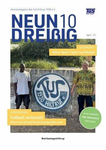 Zwei Männer stehen vor einer Wand mit dem Logo des TuS Hiltrup 1930 e.V., umgeben von grüner Vegetation.