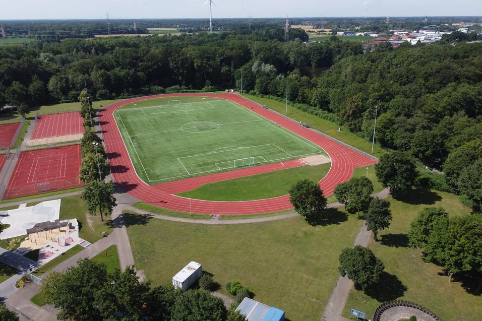 Luftaufnahme eines Sportgeländes mit einem Fußballfeld, Tennisplätzen und umliegendem Wald.