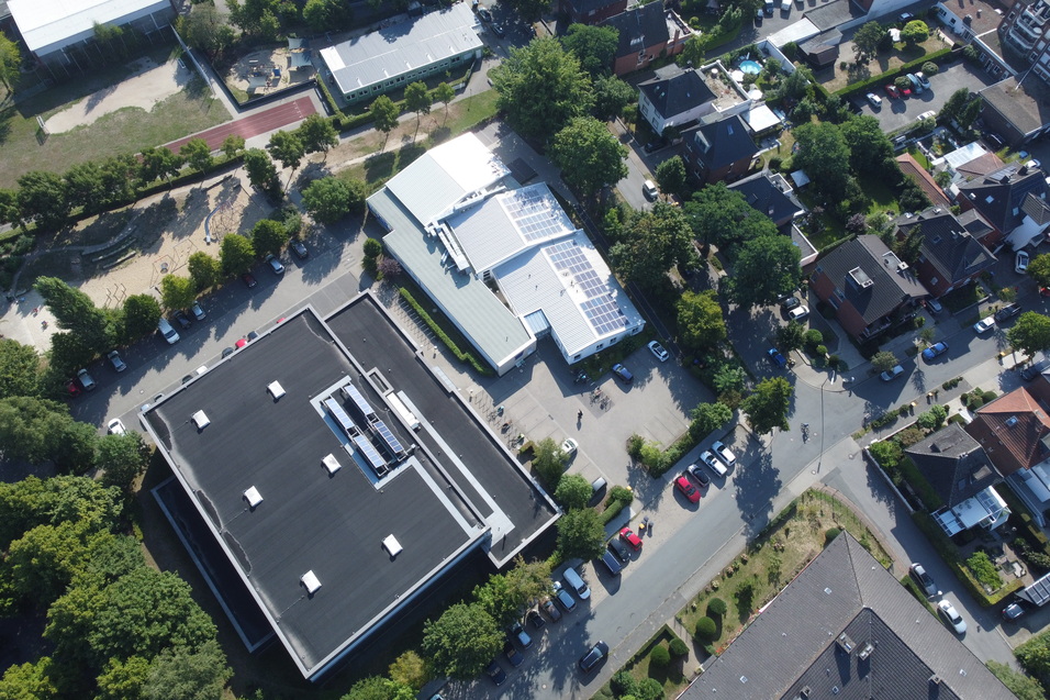 Luftaufnahme eines Wohngebiets mit Schulen, Spielplatz, Parkpl&auml;tzen und angrenzenden Wohnh&auml;usern.