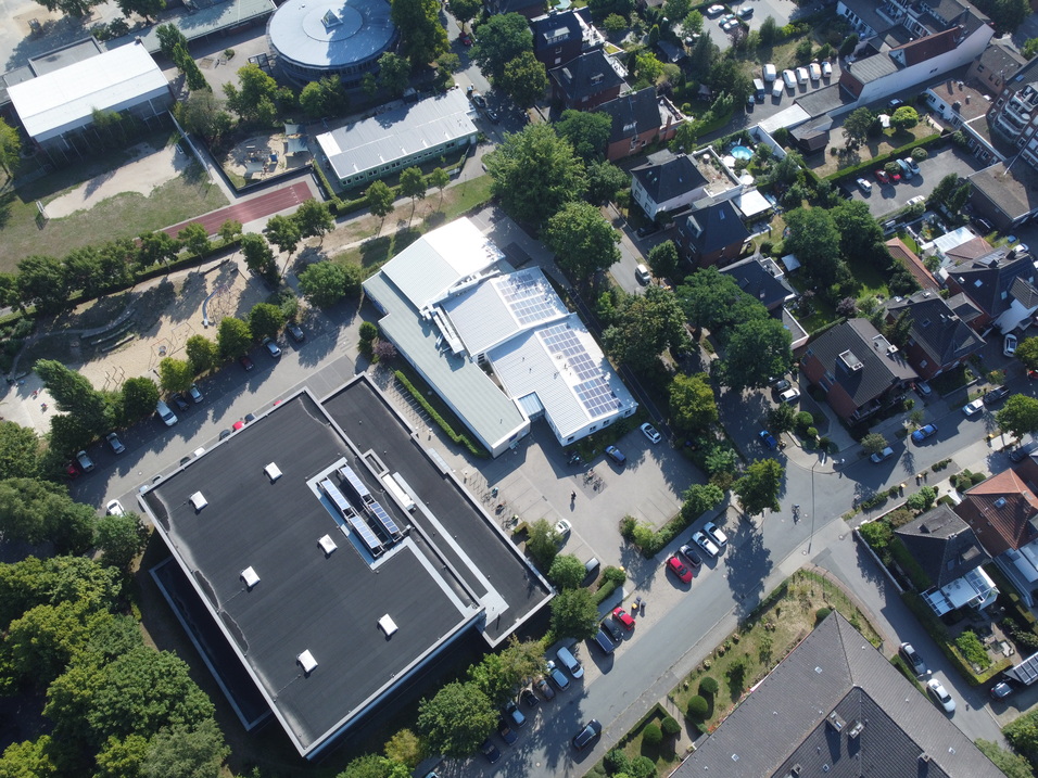 Luftaufnahme eines Wohngebiets mit Schulen, Spielplatz, Parkplätzen und angrenzenden Wohnhäusern.