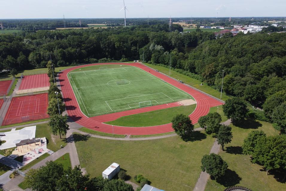 Luftaufnahme eines Sportgeländes mit einem Fußballfeld, Tennisplätzen und umliegendem Wald.