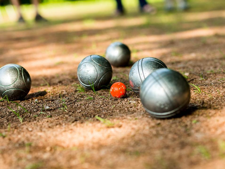 Gleise mit silbernen Boulekugeln und einer roten Kugel auf einem erdigen Boden in einem Park.