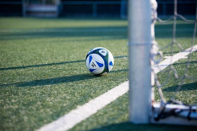 Fußball liegt auf einem Kunstrasenplatz, nahe einem Torpfosten mit Netz.