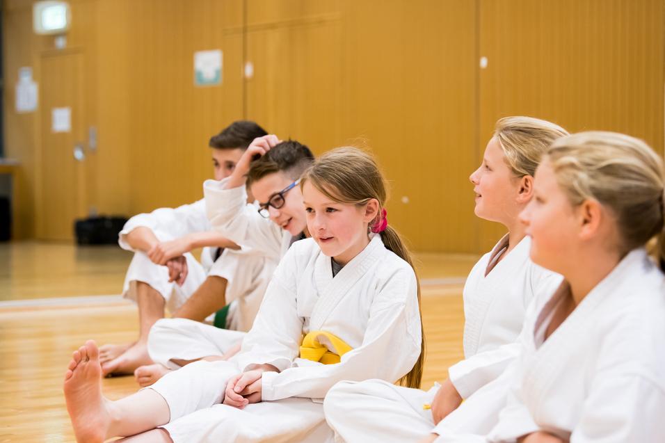 F&uuml;nf Kinder in wei&szlig;en Anz&uuml;gen sitzen in einer Trainingshalle.
