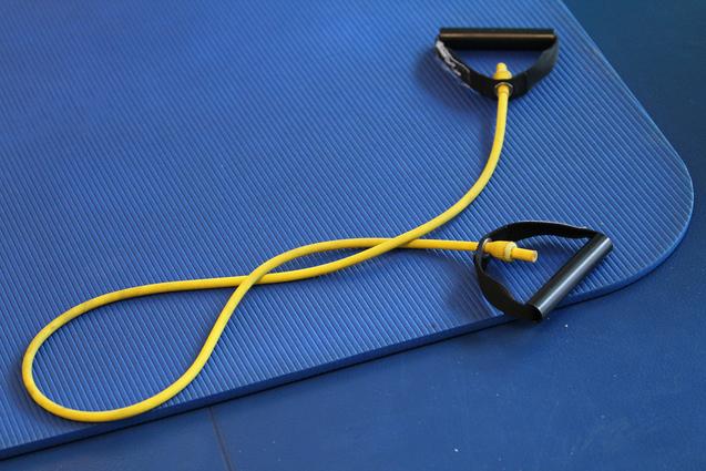 Gelbes Widerstandsband mit schwarzen Griffen auf einer blauen Gymnastikmatte.