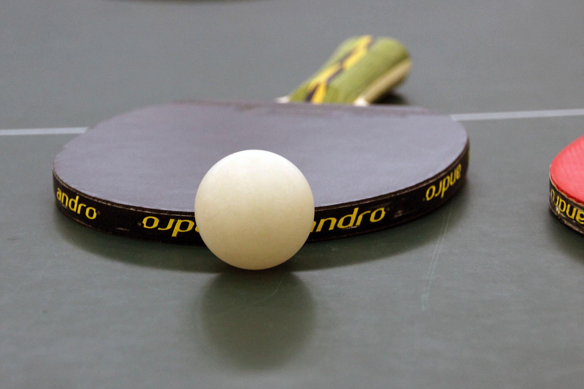 Nahaufnahme eines Tischtennisschlägers mit weißem Ball auf einer grünen Tischtennisplatte.
