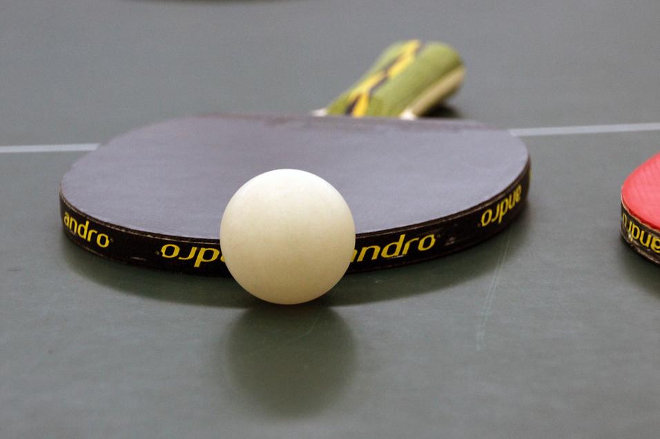 Nahaufnahme eines Tischtennisschlägers mit weißem Ball auf einer grünen Tischtennisplatte.